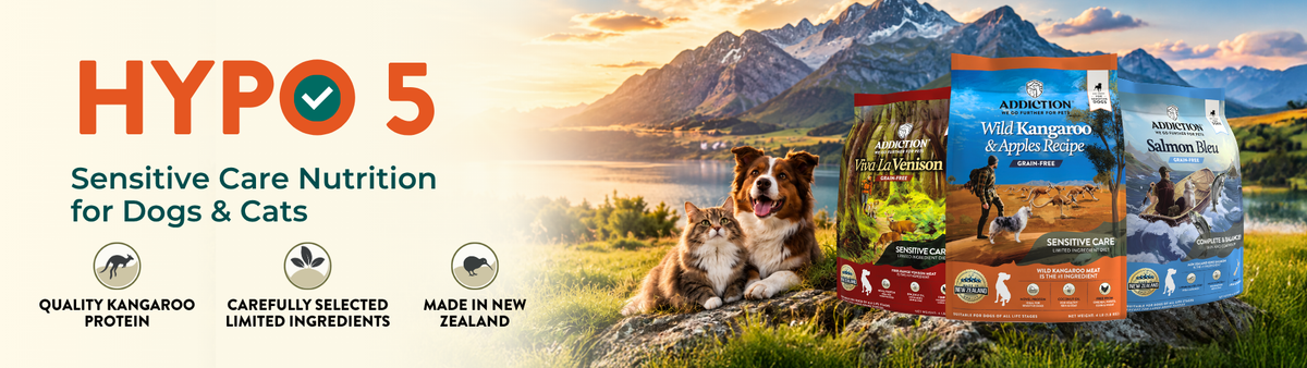 Hypo 5 Sensitive Care Nutrition dog food packaging shown against a scenic outdoor background with a mountain lake landscape and a dog lying on a log. The packages are for wet and dry dog food in blue, green, and orange flavors.